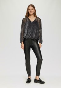 Zwarte, doorschijnende blouse met lange mouwen en een textuurafwerking, gecombineerd met strakke zwarte imitatieleren broek en glanzende zwarte loafers.
