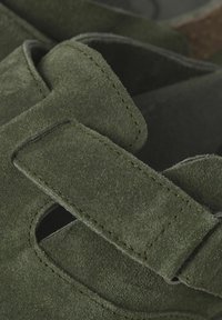 Sandal de ante verde con una correa de Velcro, costuras detalladas y secciones recortadas para mayor transpirabilidad. La superficie texturizada añade profundidad.