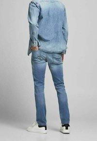 Jeans de mezclilla azul claro con un diseño ajustado, que cuentan con bolsillos traseros y un ligero desgaste. Combinados con una camisa de mezclilla y zapatillas blancas.