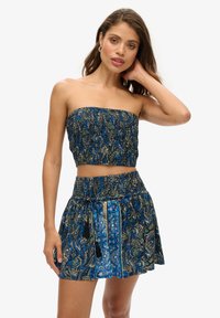 Ensemble bi-matière bleu à motifs comprenant un haut smocké sans bretelles et une jupe assortie avec un cordon de serrage et des pompons.