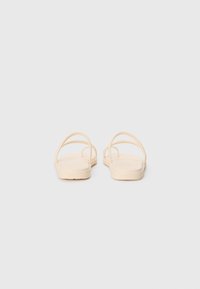 Light beige sandals with thin, crisscross straps and a flat sole. Made of soft, flexible material, featuring a minimalistic design.