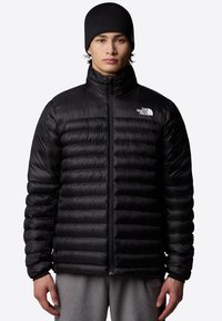 Črna puhovka z vodoravno prešitim vzorcem, sprednjim zadrgo, visokim ovratnikom in logotipom The North Face na levem prsnem delu.