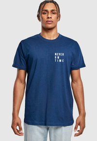Marineblå bomulds t-shirt med korte ærmer og rund hals. Hvid tekst "ALDRIG TIL TIDEN" trykt på forsiden. Regular fit design.