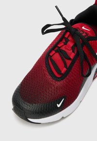 Röd nätatletikskor med svarta accentfärger, texturerat tåparti och svarta snören. Har en vit Nike-logotyp på sidan och en slät sula.