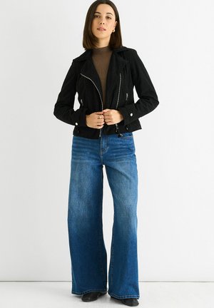 Black corduroy jacket with a zip front and silver hardware, paired with wide-leg blue jeans in a gradual color transition from dark to light.
