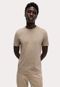 Camiseta de manga corta beige, hecha de suave tejido de algodón, con escote redondo y un corte relajado. Diseño minimalista sin patrones.
