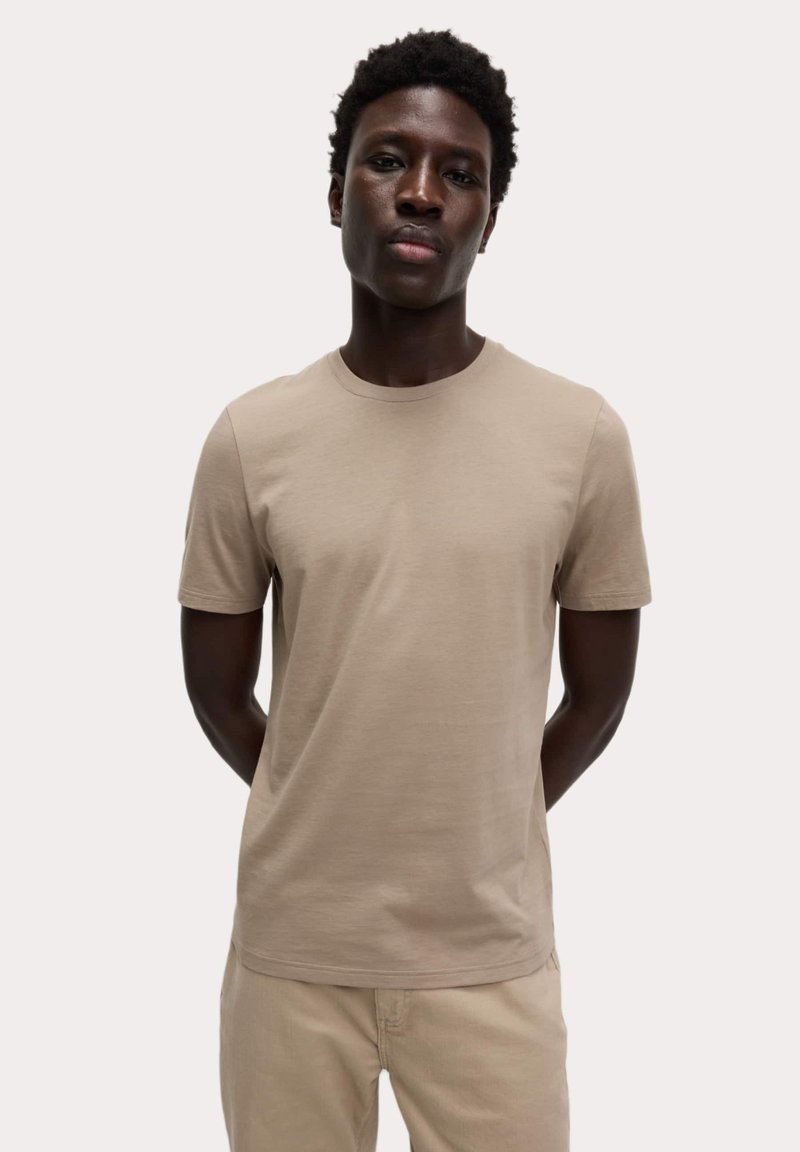 Camiseta de manga corta beige, hecha de suave tejido de algodón, con escote redondo y un corte relajado. Diseño minimalista sin patrones.