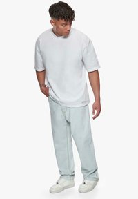 Hvid bomulds T-shirt med korte ærmer, sat sammen med lyseblå store jeans. Hvide sneakers fuldender outfittet. Enkel, afslappet design.