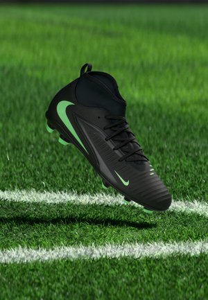 Chaussure de football Nike noire et vert néon flottant au-dessus d’une pelouse verte avec des lignes blanches sur le terrain.