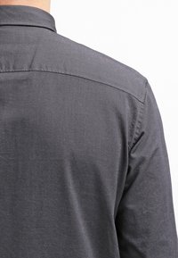 Camicia grigia in cotone con una texture morbida, caratterizzata da un colletto classico e un yoke cucito sulle spalle, vista da dietro.