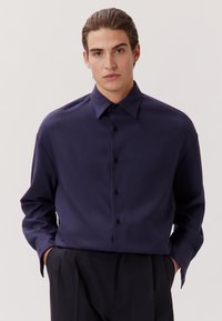 Navyblaues Langarmhemd mit durchgehender Knopfleiste, klassischem Kragen und einem glatten, leicht strukturierten Stoff. Mit schwarzen Knöpfen.