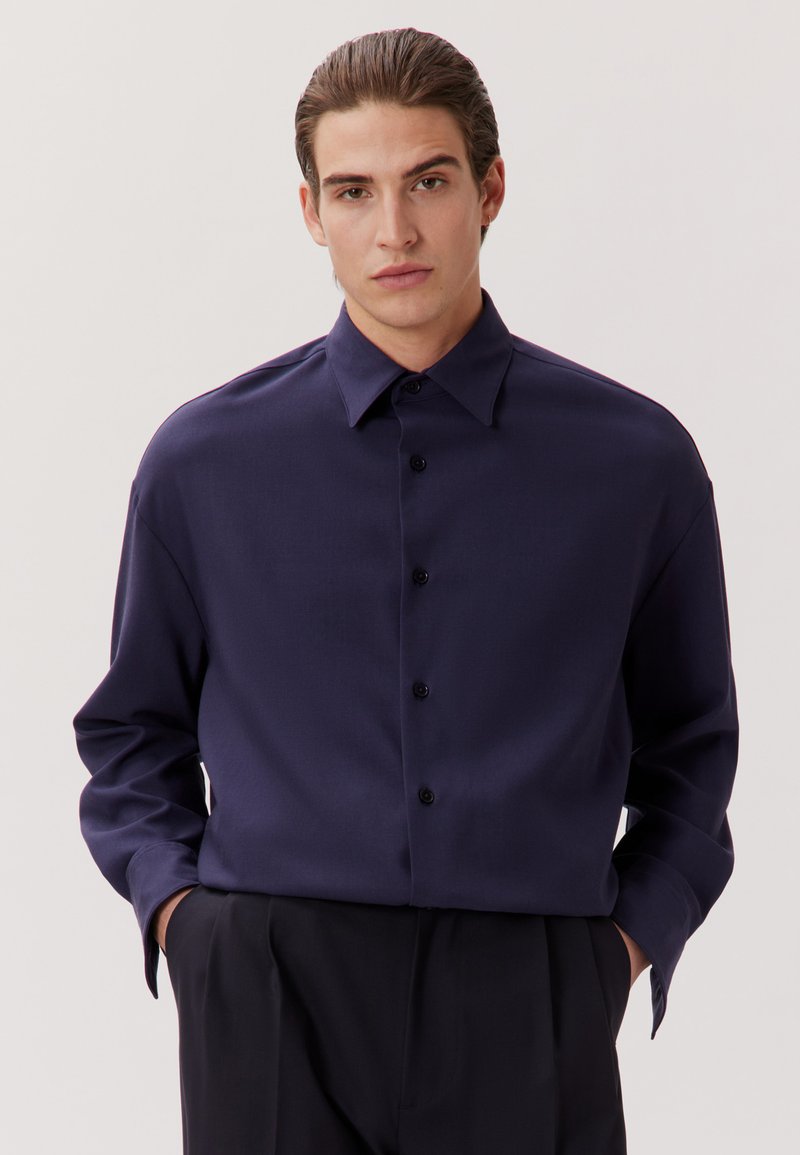 Navyblaues Langarmhemd mit durchgehender Knopfleiste, klassischem Kragen und einem glatten, leicht strukturierten Stoff. Mit schwarzen Knöpfen.