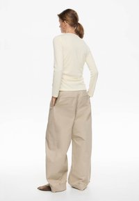 Top de manga larga color crema claro con ajuste ceñido y textura suave, combinado con pantalones oversized beige que cuentan con bolsillos laterales y dobladillos abotonados.