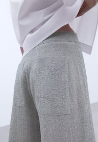 Grijze geprinte broek van een textured stof, met twee achterzakken en een aansluitende tailleband, gecombineerd met een witte top.