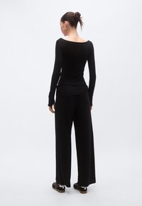 Μαύρο μπλουζάκι με μακριά μανίκια και μπούστο με σκάφος, συνδυασμένο με φαρδιά μαύρη παντελόνα. Και τα δύο ρούχα είναι κατασκευασμένα από λείο, ελαστικό ύφασμα.