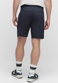 Marinblå linnebyxor med två bakfickor, knappdetaljer och ren nederkant. Bärs med svartvita randiga strumpor och grå sneakers.