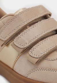 Beidzis zamšādas sneakers ar trim regulējamiem āķu un cilpu siksnām un brūnu gumijas zoli, tuvplāna attēls ar tekstūras un šuvju detaļām.