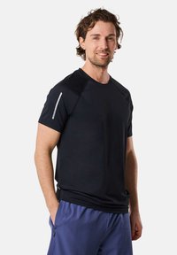 Zwarte sportieve t-shirt met korte mouwen, raglan ontwerp, soepele textuur, benadrukt met een reflecterende streep op de linker schouder.