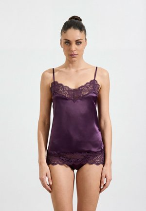 Woman standing facing forward wearing purple satin camisole and matching lace-trimmed shorts against a plain white background.