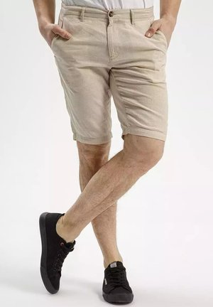 Beige shorts with a smooth texture, featuring front pockets and a button closure, paired with black sneakers.