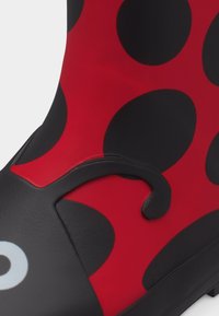 Κοντινό πλάνο κόκκινου και μαύρου αδιάβροχου μποτάκι με θέμα πασχαλίτσας, με μαύρες κηλίδες και μαύρη λαβή στο πλάι.