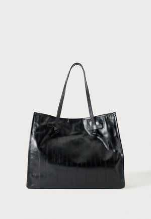 Borsa tote in pelle nera lucida con due sottili spalline e una sottile texture verticale su sfondo chiaro e uniforme.