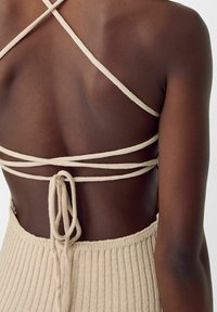 Beige stickad crop top med tunna korsettsnor och knytning på baksidan, med ribbat mönster och minimalistisk design.