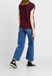 Burgundy kortærmet top kombineret med brede blå jeans og sorte højtop sneakers. Stoffet ser blødt ud og har en afslappet pasform.