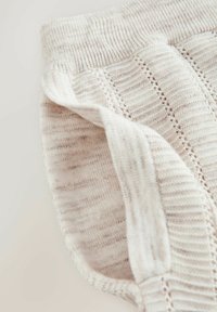 Gros plan sur un tissu tricoté beige doux avec un poignet côtelé et des motifs de points verticaux texturés.