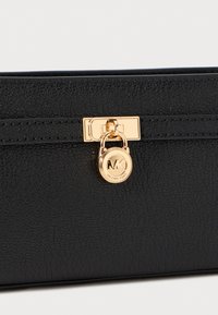 Black leather wallet with a textured finish, featuring a gold clasp and a circular charm with a logo, essential for secure closure.