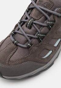 Scarpa da trekking grigia con una combinazione di rete testurizzata e suede liscio, con accenti blu e un sistema di allacciatura complesso.