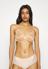 Persiku krāsas mežģīņu bralette ar regulējamām siksnām, ziedu rakstu un apakšējo stiepšanu. Atbilstošās biksītes piedāvā mežģīņu akcentus un gludu apdari.