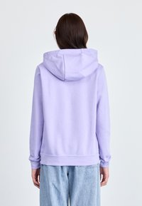 Sweat à capuche violet en tissu doux. Présente des manches longues, une capuche avec cordon de serrage et des poignets côtelés, associé à un jean bleu clair.