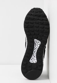 Sole di una sneaker in bianco e nero con motivi di battistrada circolari e un dettaglio di intersuola bianca maculata su uno sfondo bianco semplice.