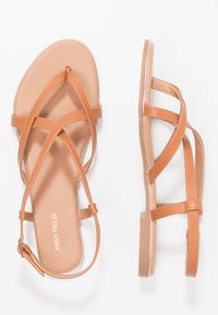 Brown leather sandals with crossed straps, flat sole, and ankle buckle. Smooth texture and minimalistic design. Brand name embossed inside.