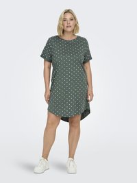 Grön kortärmad klänning med vita prickar, avslappnad passform, rundad halsringning, hög-låg fåll, tillsammans med vita sneakers.