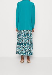 Tyrkysové sako s přizpůsobeným střihem, doplněné vzdušnou sukni s květinovým vzorem v modré a bílé barvě, dokončené světlými sandály.