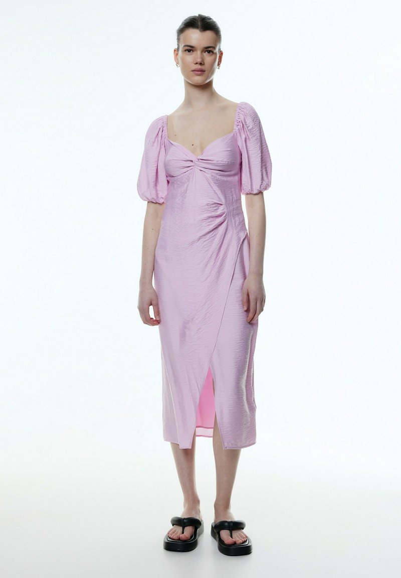 Roze midi-jurk met gebloemde mouwen, ingezamelde voorkant en een hoge splits. Textuurstof, gedragen met zwarte chunky sandalen.