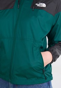 Roheline ja must kerge jope, millel on lukuga ees, elastsed mansetid ja küljetaskud. Kangas on sileda tekstuuriga ja minimaalse brändinguga.