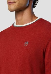Maglione rosso con collo rotondo, dotato di un colletto a coste bianco e grigio e un piccolo logo rotondo sul petto. Realizzato in un materiale morbido.