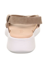 Beżowe zamszowe sandały z białą syntetyczną podeszwą, otwartym tyłem i regulowanym paskiem na kostkę. Podeszwa wewnętrzna jest gładka i lekko wyściełana.