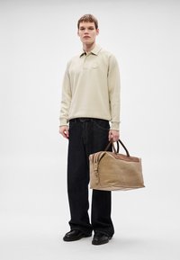 Bézs pulóver, sötét farmer, nagy barna bőrtáska barna részletekkel és lapos talppal, sima textúrával és strukturált kialakítással.