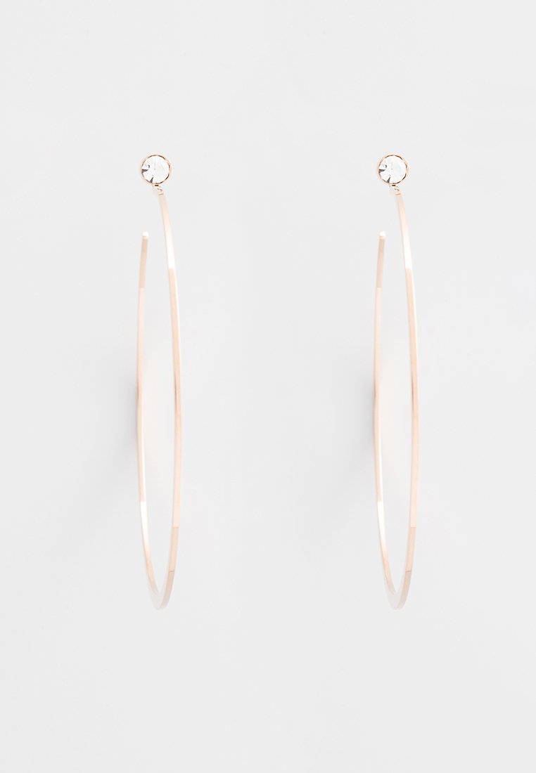 Boucles d'oreilles en or rose en forme de créoles, présentant un design fin et allongé avec un petit cristal transparent en accent en haut. Texture lisse et finition polie.