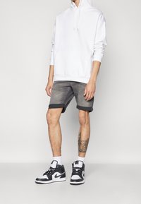 Vit hoodie med kenguruficka, grå denimshorts med uppvikt fåll, och svartvita sneakers med gröna detaljer.