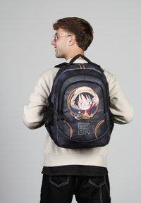 Mochila con un tejido negro texturizado, que presenta un gráfico colorido de un niño con sombrero de paja y diseño de cuerda, con costuras en contraste.