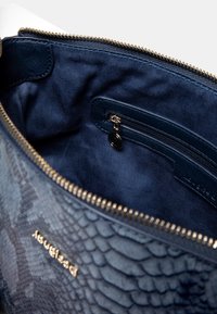 Niebieska teksturowana torebka z otwartym złotym zamkiem, ukazująca materiałową wyściółkę wnętrza oraz małą kieszonkę na suwak w środku.