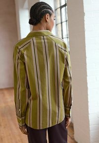 Olijfgroene gestreepte shirt met verticale witte en roze strepen, lange mouwen en knoopmanchetten, met een traditionele kraag en rugpas.