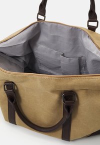 Brown canvas bag with dark leather accents, featuring an interior striped pattern, multiple pockets, and sturdy handles. Zippered closure.