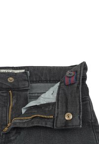 Mörkgrå jeans med en mässingsdragkedja, metallknapplåsning och kontrasterande tyg i midjan. Har ett röd- och blårandigt accent.