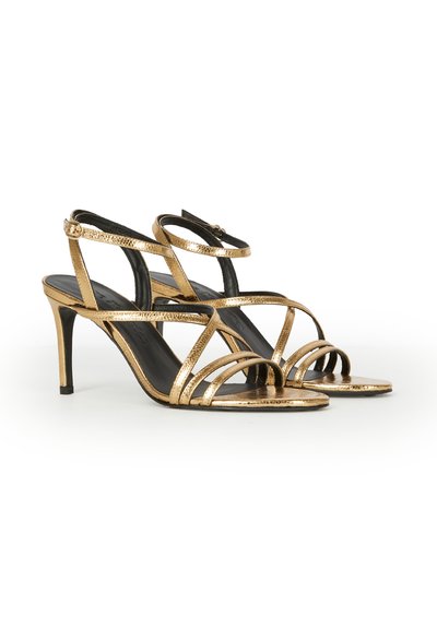 Metallic gold strappy high-heeled sandals with ankle buckle, open toes, and slender heels on a white background.